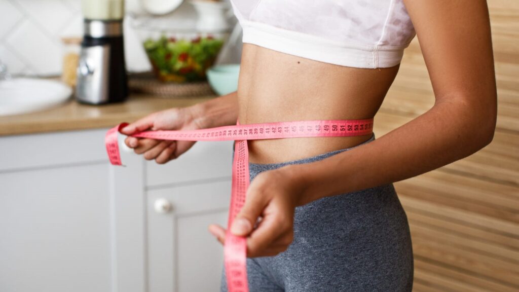 Vrouw meet haar taille met een roze meetlint na het padel, zichtbaar in sportkleding