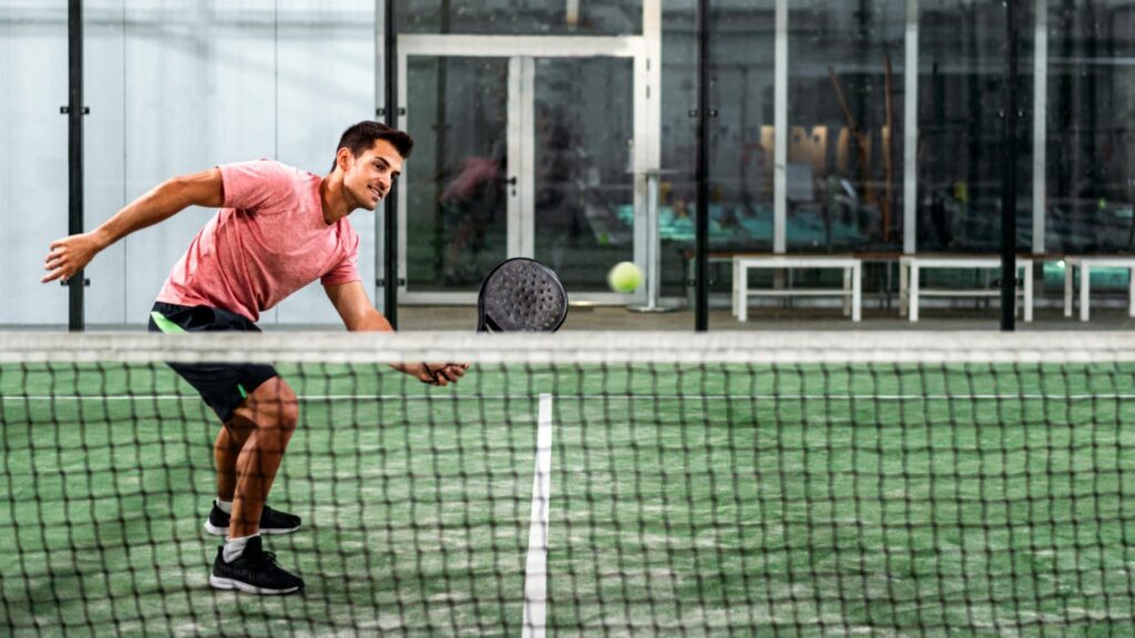 Man in sportkleding die geconcentreerd een padelwedstrijd speelt op een indoorbaan