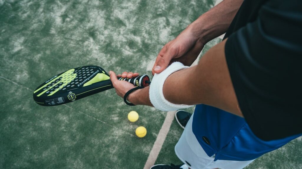 Padelspeler met racket en polsband op kunstgrasbaan, klaar voor een potje met geschikte racketsportschoenen.