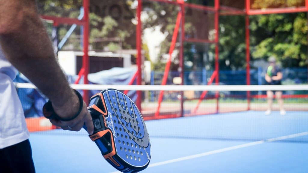 Speler houdt padelracket vast op een blauwe baan, ideaal moment om een padel cadeau in actie te zien.