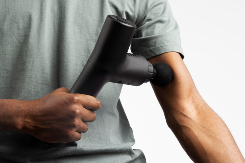 Man gebruikt een massage gun op zijn bovenarm voor spierherstel en fit blijven in de winter