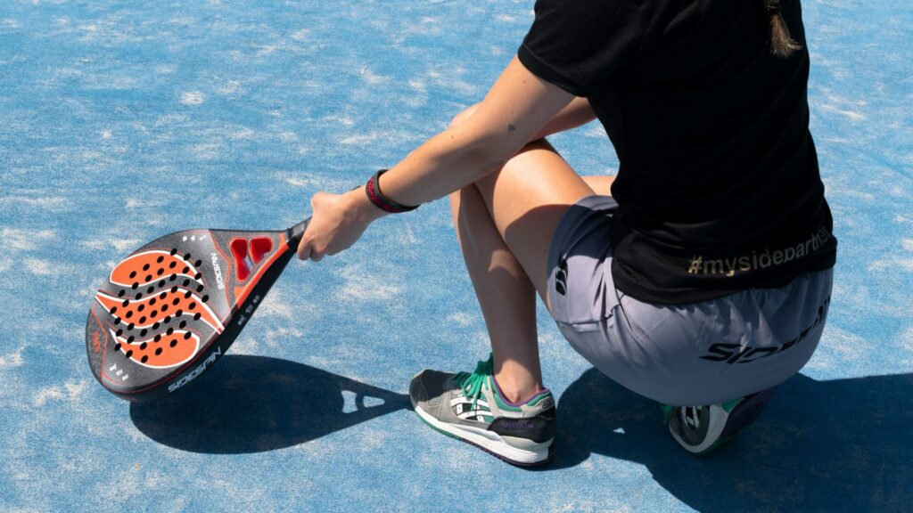 Padelspeler in sportoutfit op blauwe baan met racket en stevige padelschoenen die grip en steun bieden.