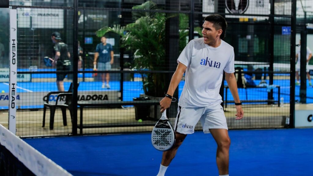 Speler in actie op indoor padelbaan tijdens evenement met meerdere deelnemers.