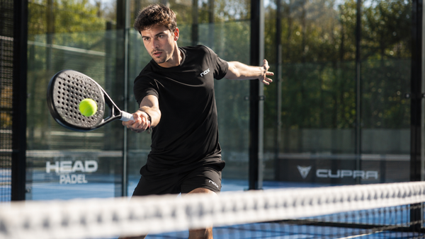 Man slaat een bal tijdens een intensieve padelwedstrijd op een outdoor padelbaan