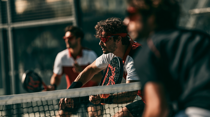Twee padel spelers in sportkleding met zonnebril en padel racket gereed bij het net tijdens een intensieve padelwedstrijd.