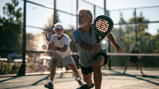 Twee actieve senioren spelen een dynamische wedstrijd padel op een buitenbaan in de zon